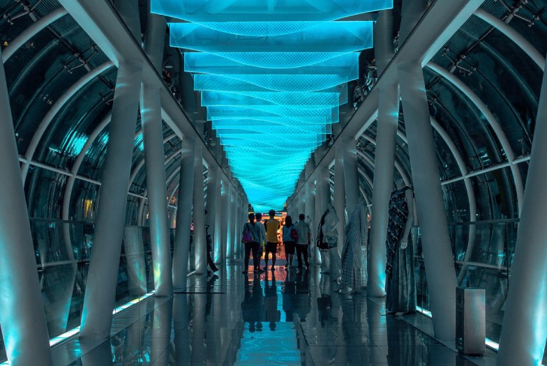 People in the middle of a a futuristic hallway lit by a bright blue ceiling.