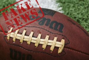Football photo of a an American foot ball on grass with the words Fake News stamped across the image.
