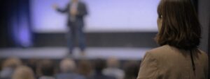 Brett Wiskar Speaker on stage watched by Speaker Bureau Account Manager