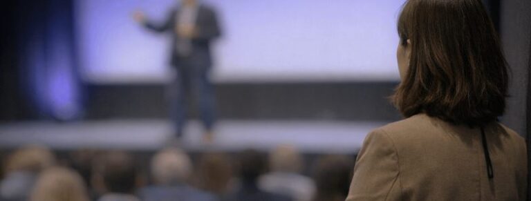 Brett Wiskar Speaker on stage watched by Speaker Bureau Account Manager
