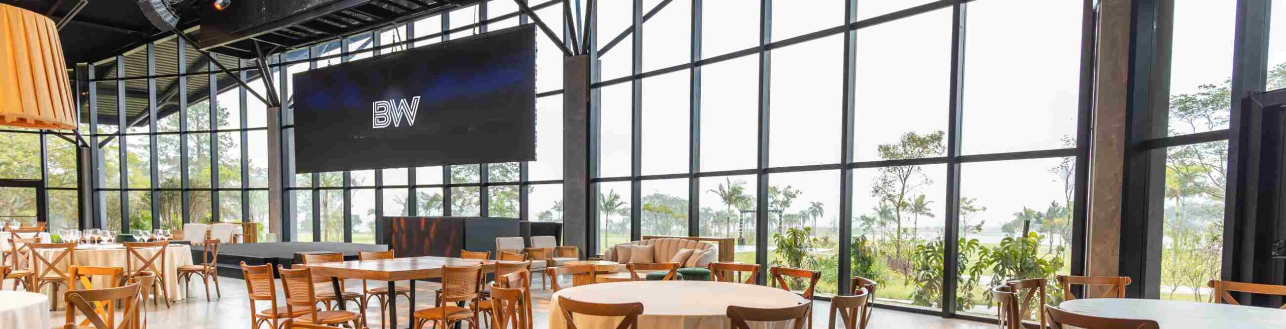 Event venue ready for conference keynote to start. Tables ready for delegates with a large screen and stage and glass wall over looking parklands. Photo by Matheus Bertelli from Pexels.